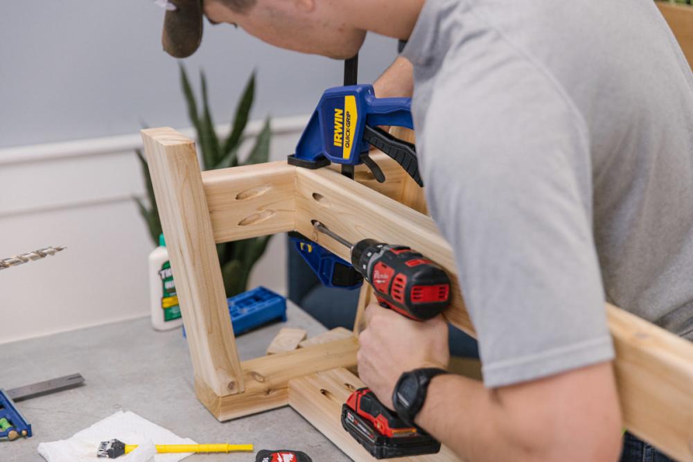 Drilling to attach a cedar decking board to the spreader of a leg assembly.