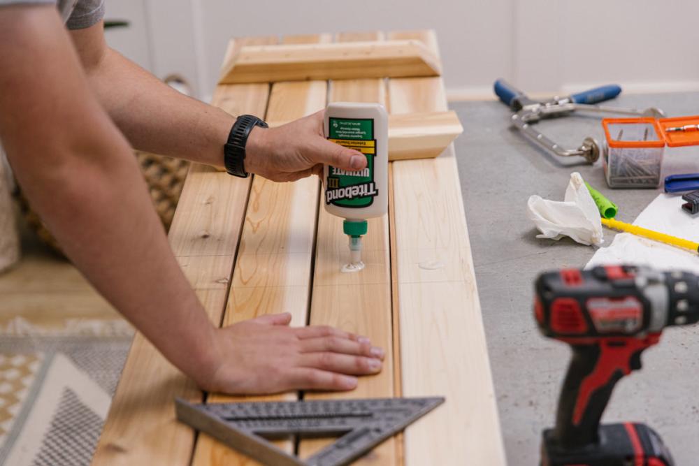 Applying wood glue in a line with one spot on each of the four bench top boards.