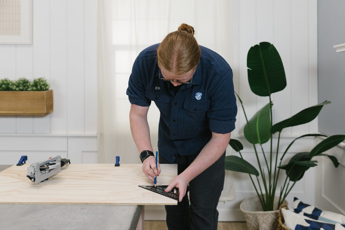 Measuring and marking ACX plywood, which is clamped to the table, before cutting it. 