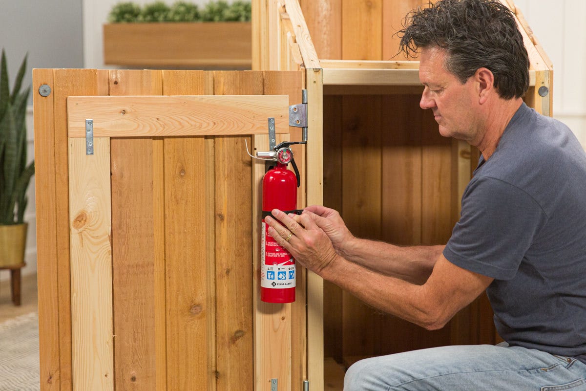 Attaching fire extinguisher to inside of door of DIY wooden outdoor cook station assembly.
