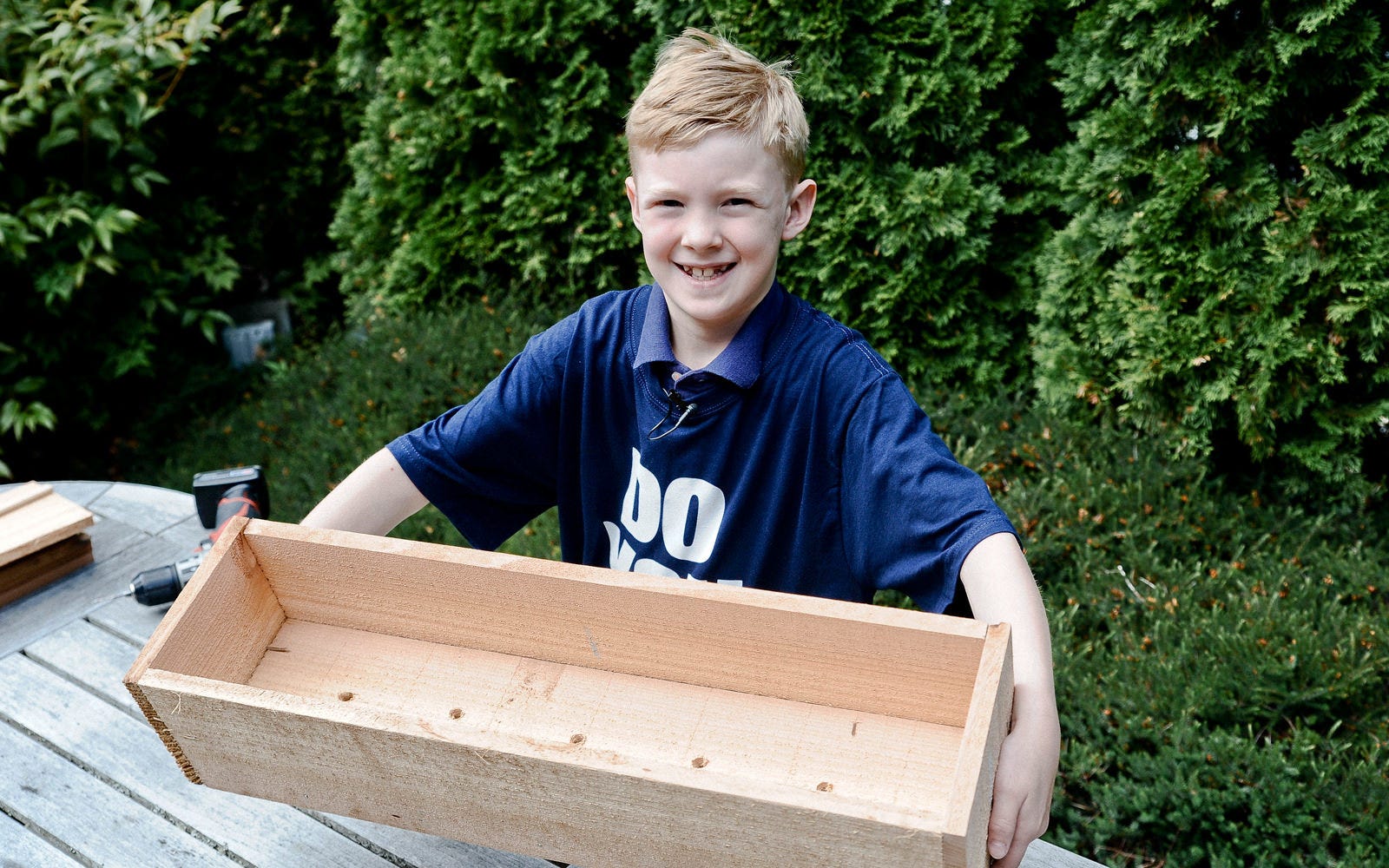 Smiling kid holding DIY wooden flower box.