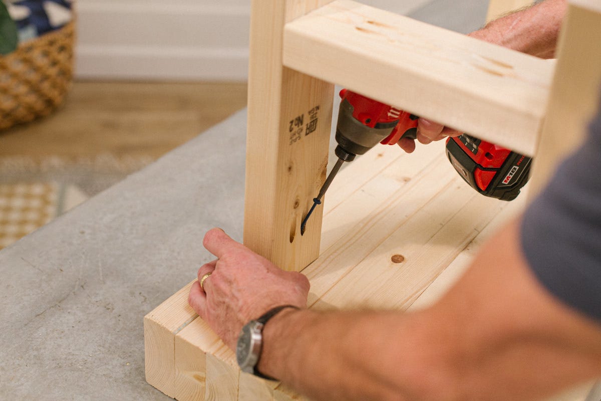 Driving screw with power drill to attach leg assembly to wood DIY outdoor bench top assembly.
