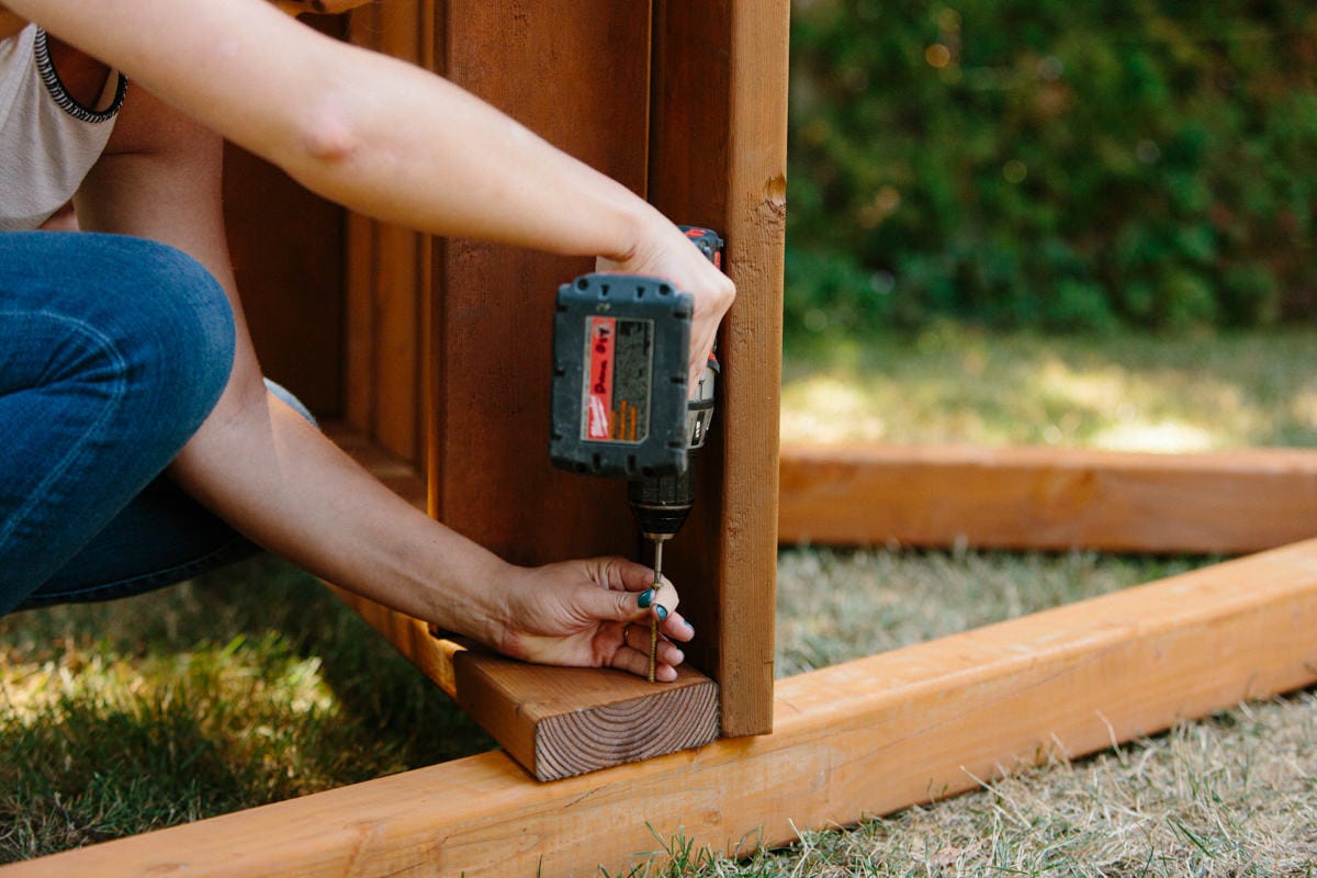 Driving screw with power drill to attach side of DIY wooden swing set platform assembly to side of A-frame.