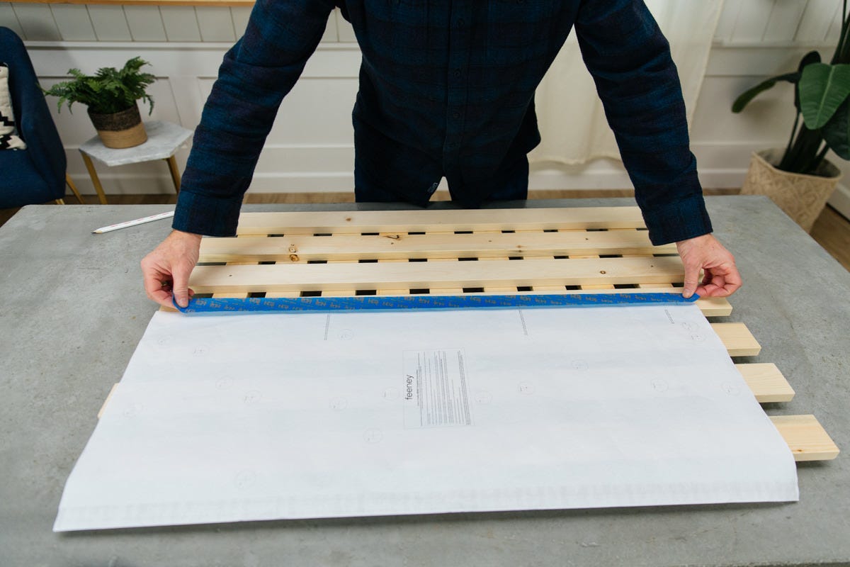 Taping DIY stainless steel garden trellis template to wall.