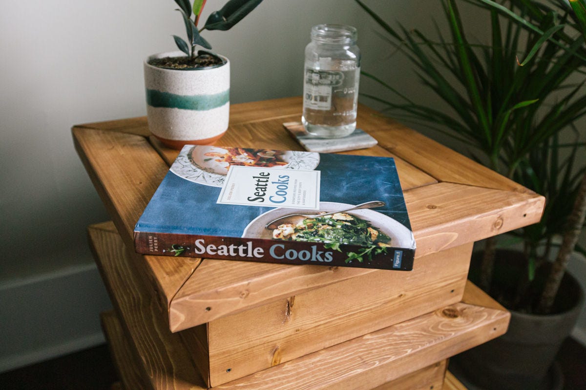 DIY wooden end table with a cookbook, potted plant and jar of water on top.