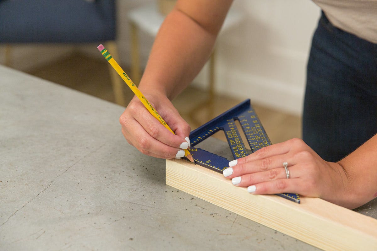 Measuring and marking white wood board with speed square and pencil.