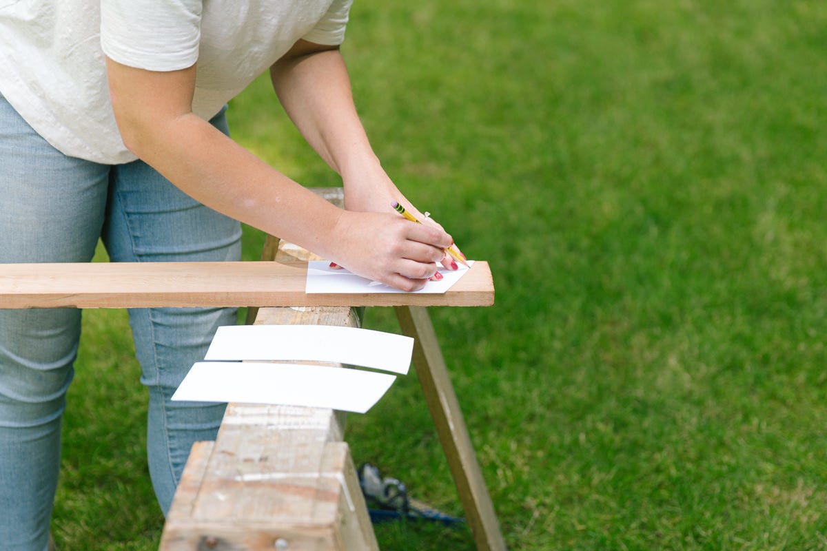 Tracing paper stencil for DIY wooden lounge chair back slats on cedar board balanced on sawhorses.