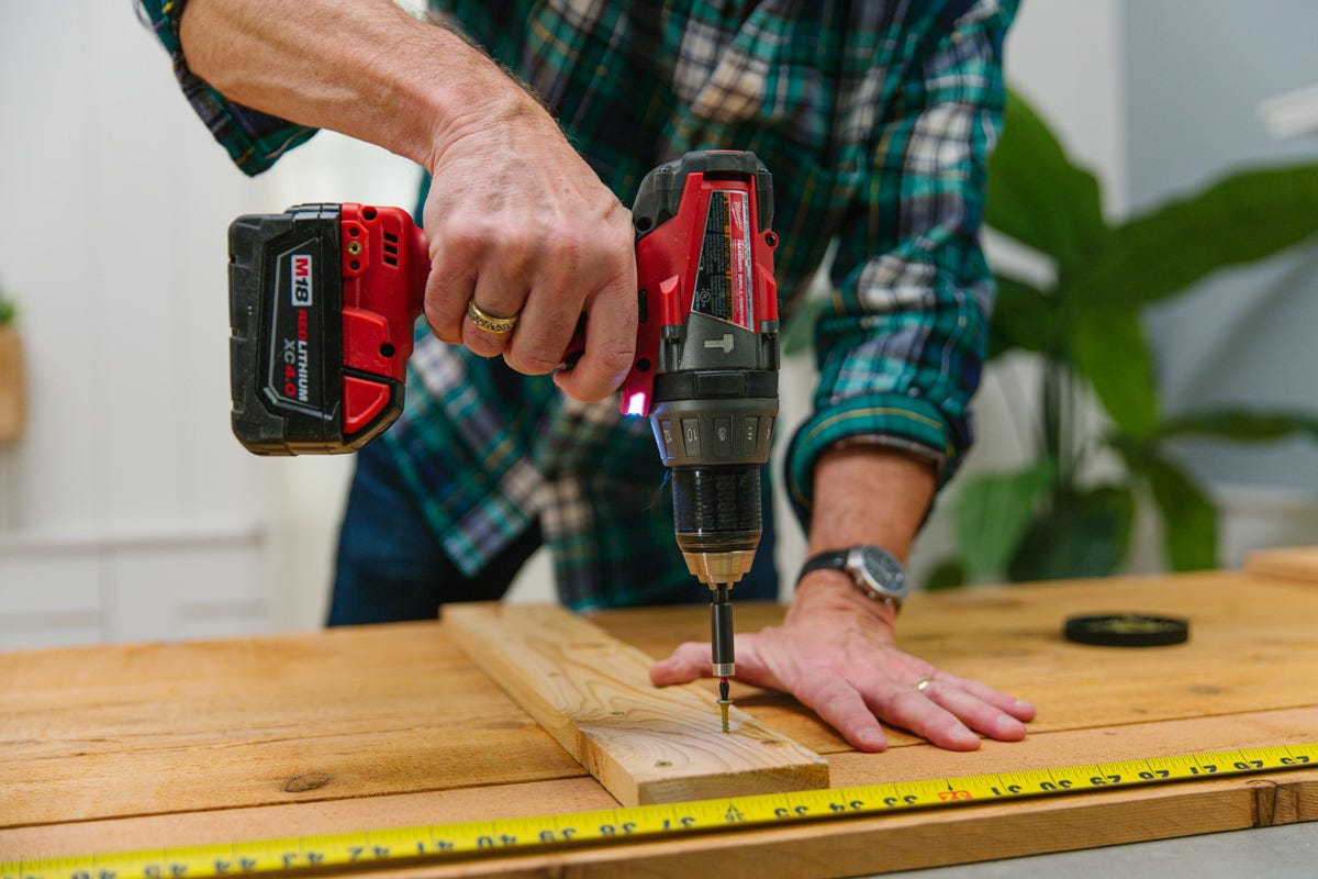 Driving screw with power drill to attach horizontal crossbar to DIY wooden garden storage shed door assembly.