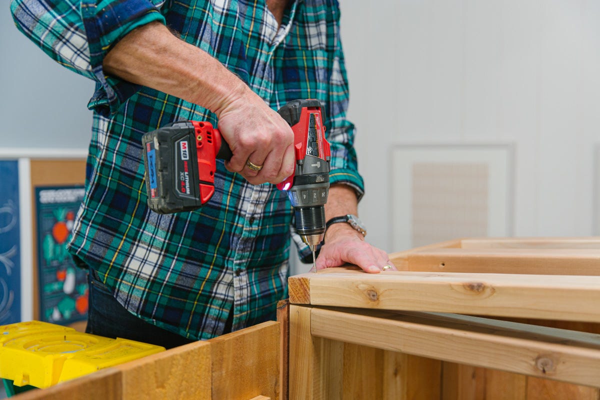 Driving screws with power drill to attach roof frame to DIY wooden garden storage shed assembly.