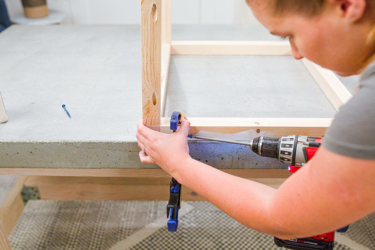 Driving screw into pocket hole in clamped DIY wooden outdoor side table base assembly to attach side frame.