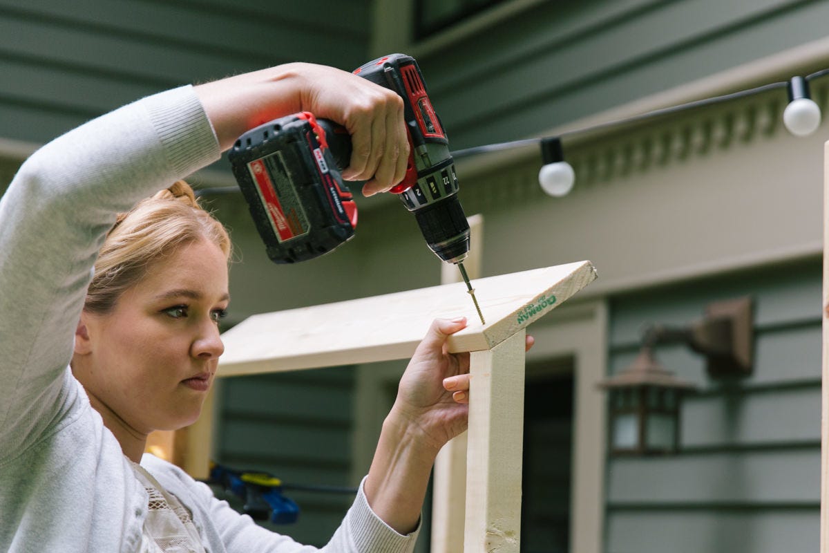 Driving screw with power drill to attach front roof support board to DIY wooden Tiki bar assembly.