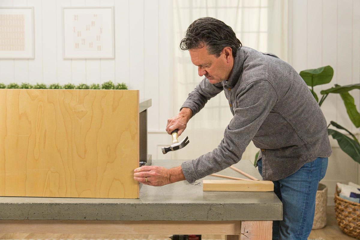 Hammering nail to attach screen mould to edge of DIY desk and sideboard organizer assembly.